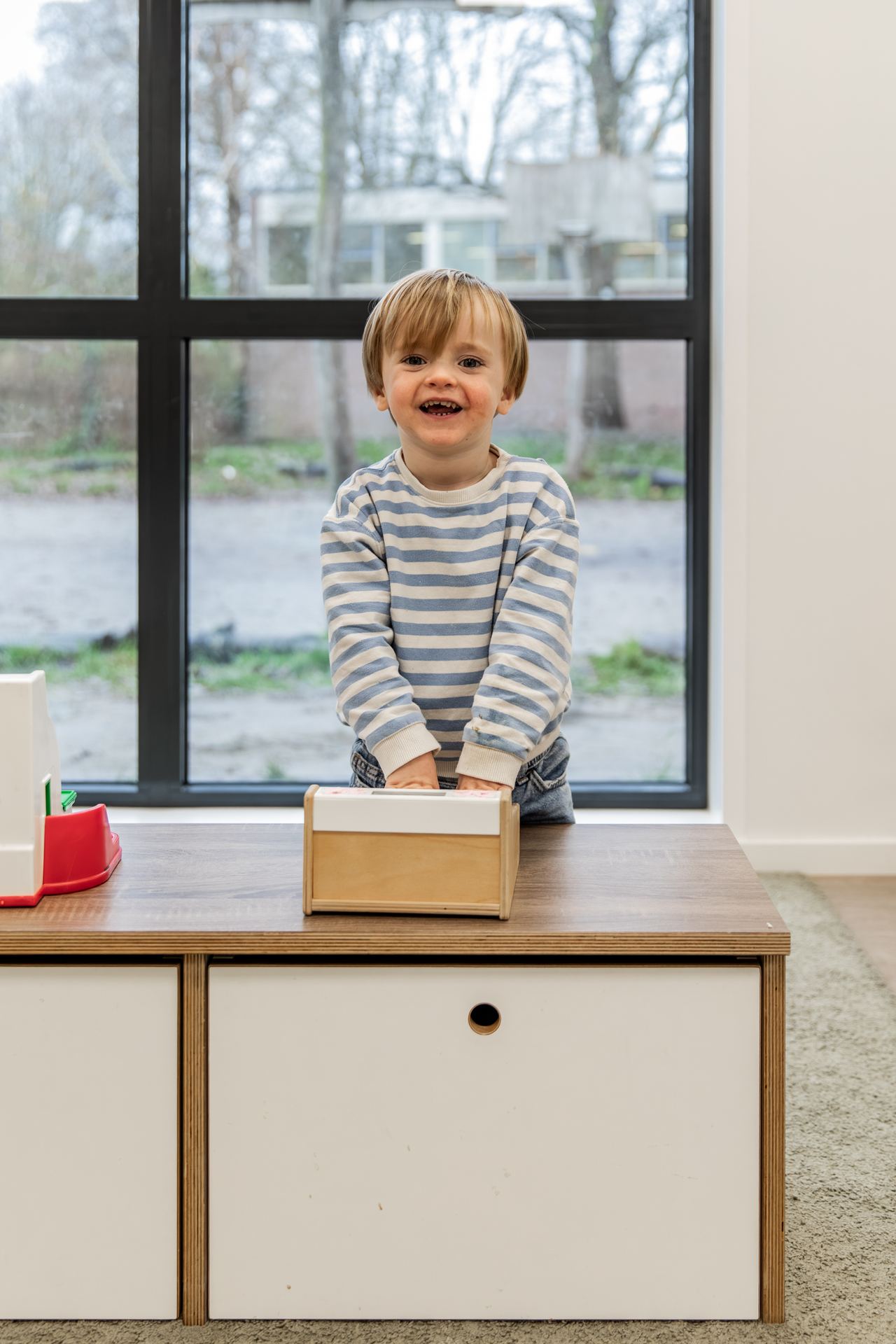 Een lachende dreumes bij het raam op het kinderdagverblijf