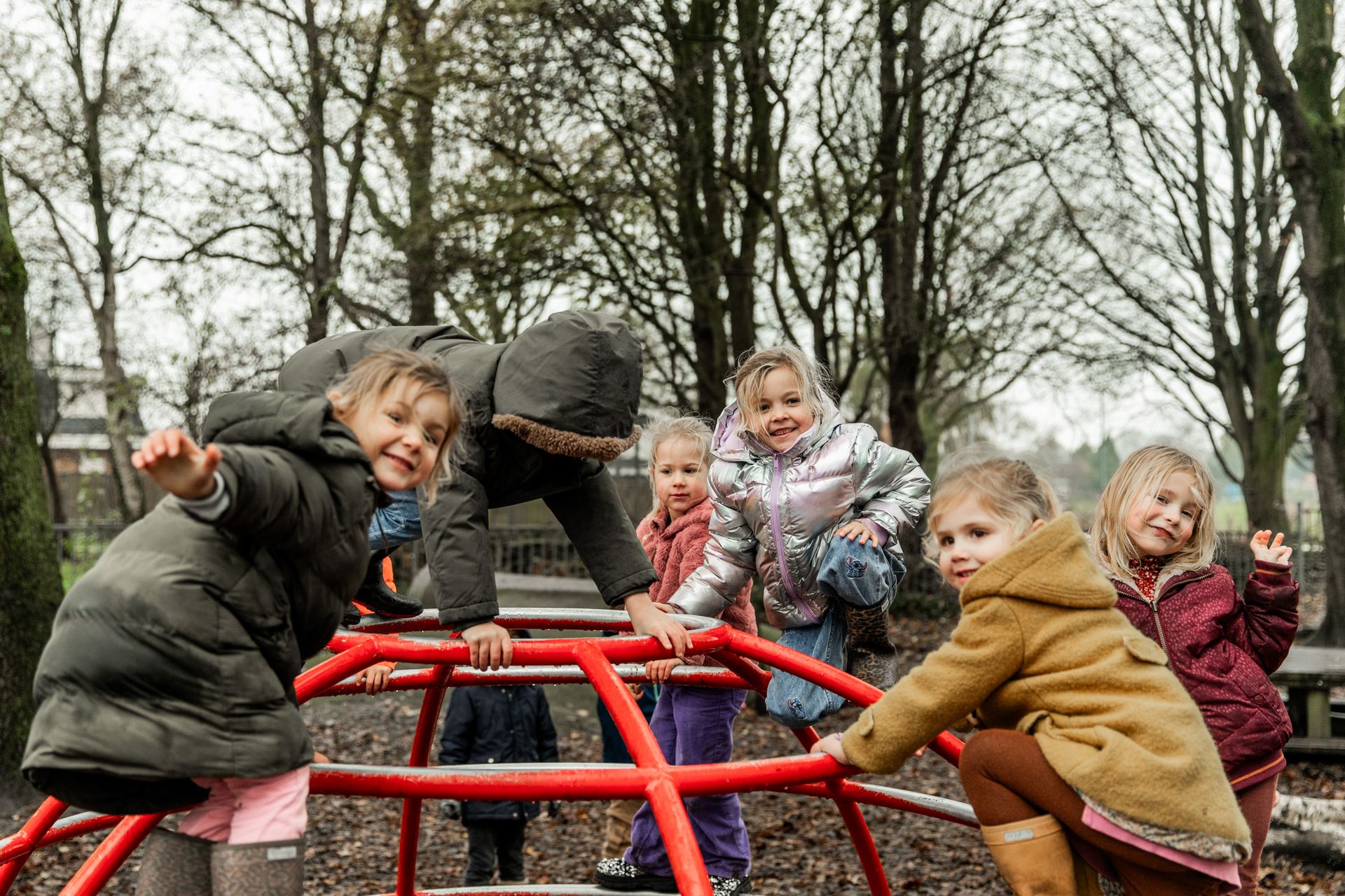 Kleuters klimmen op het rode klimrek tussen de bomen