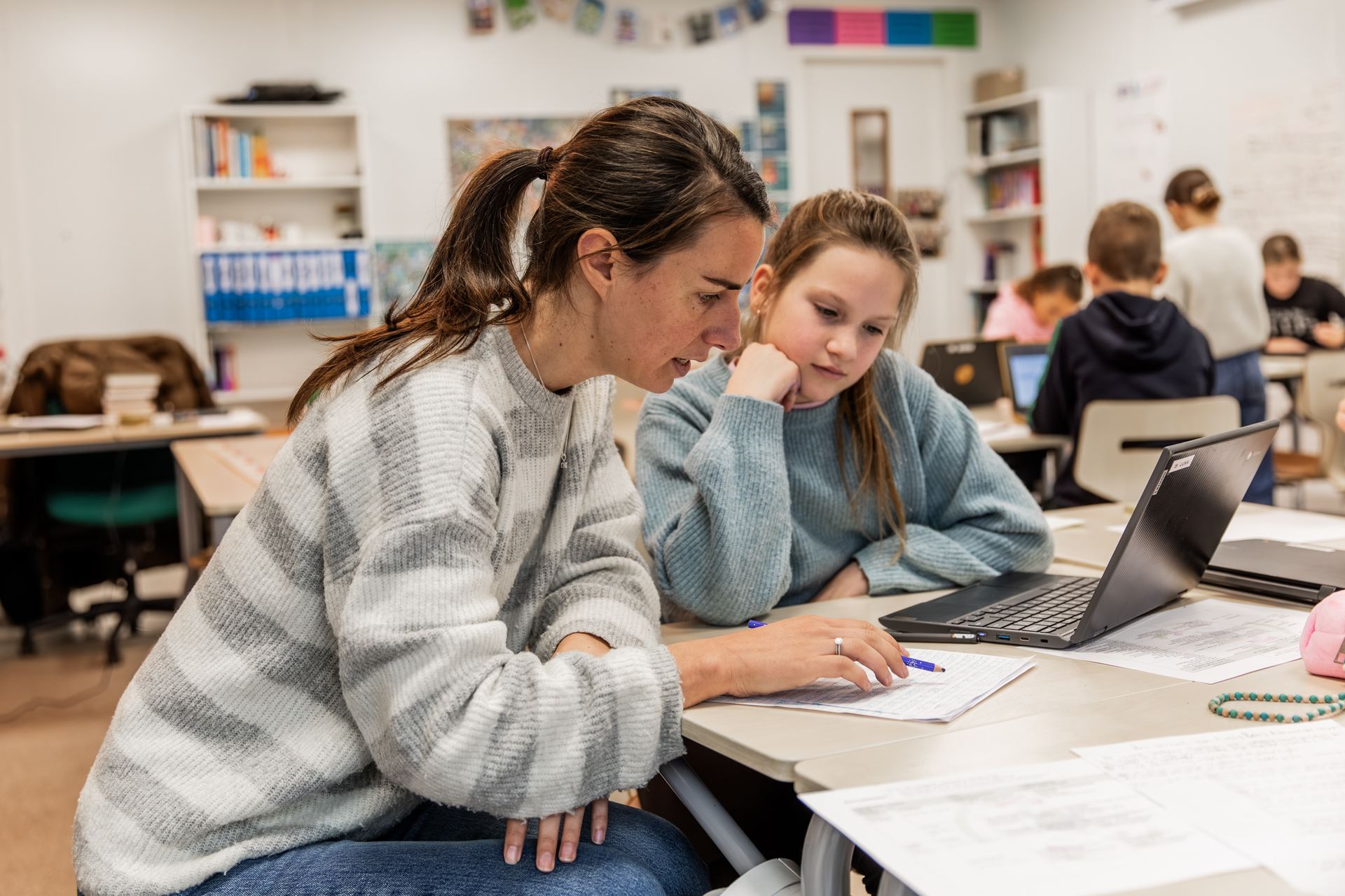 Een leerkracht helpt een leerling bij haar opdracht