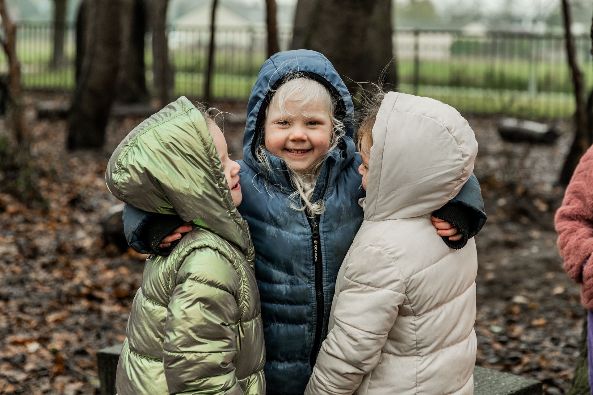 Drie lachende peuters in winterjassen in het bos