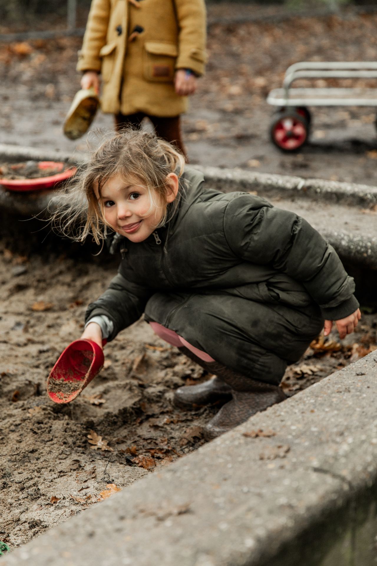 Een kleuter graaft met een schepje in de zandbak